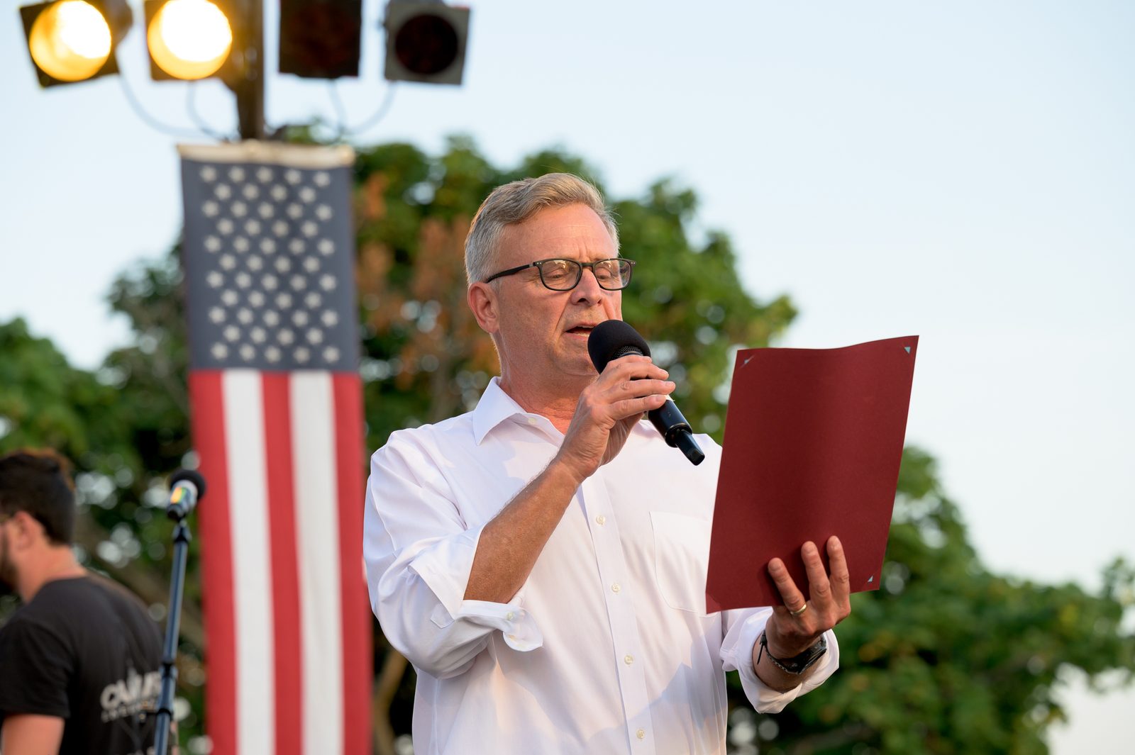 Select Board member Moses Grader reads a proclamation beneath an American flag hung from the lighting rig.