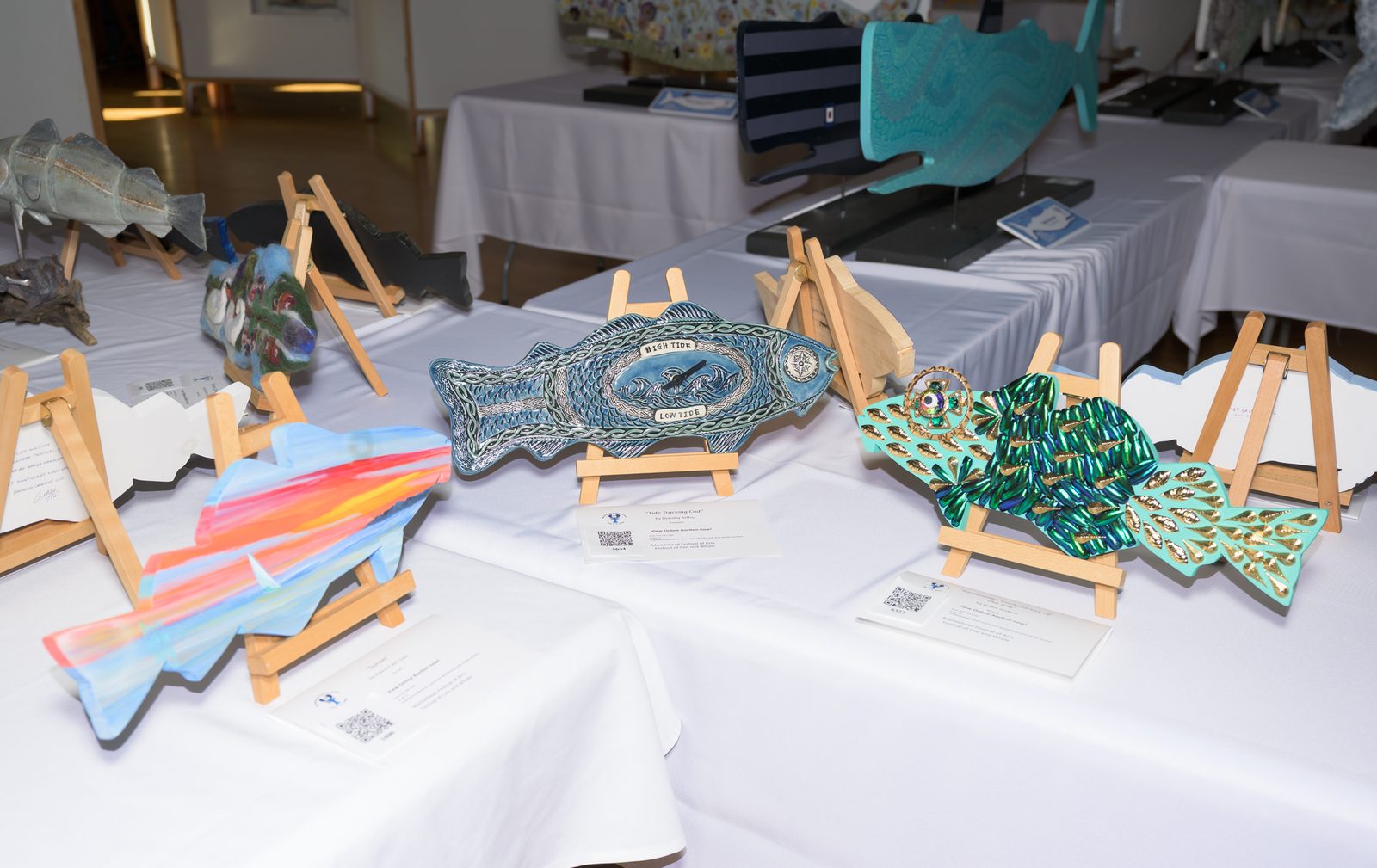 Decorated cod cutouts, including a Celtic-patterned tide clock, line the auction tables at the festival’s Festival of Cod and Whale exhibit.