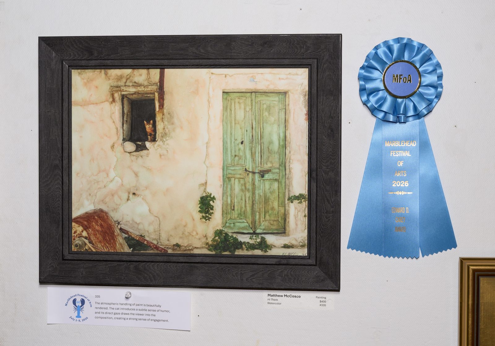 Matthew McCosco’s watercolor ‘Hi There,’ a tabby cat peering from a stone window, hangs beside the Edward D. Carey Award ribbon.