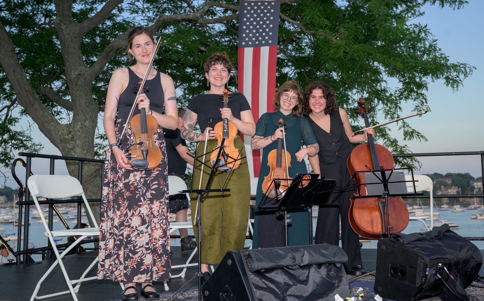 A string quartet gathers for a portrait with violins, viola and cello on the waterfront stage as dusk settles.