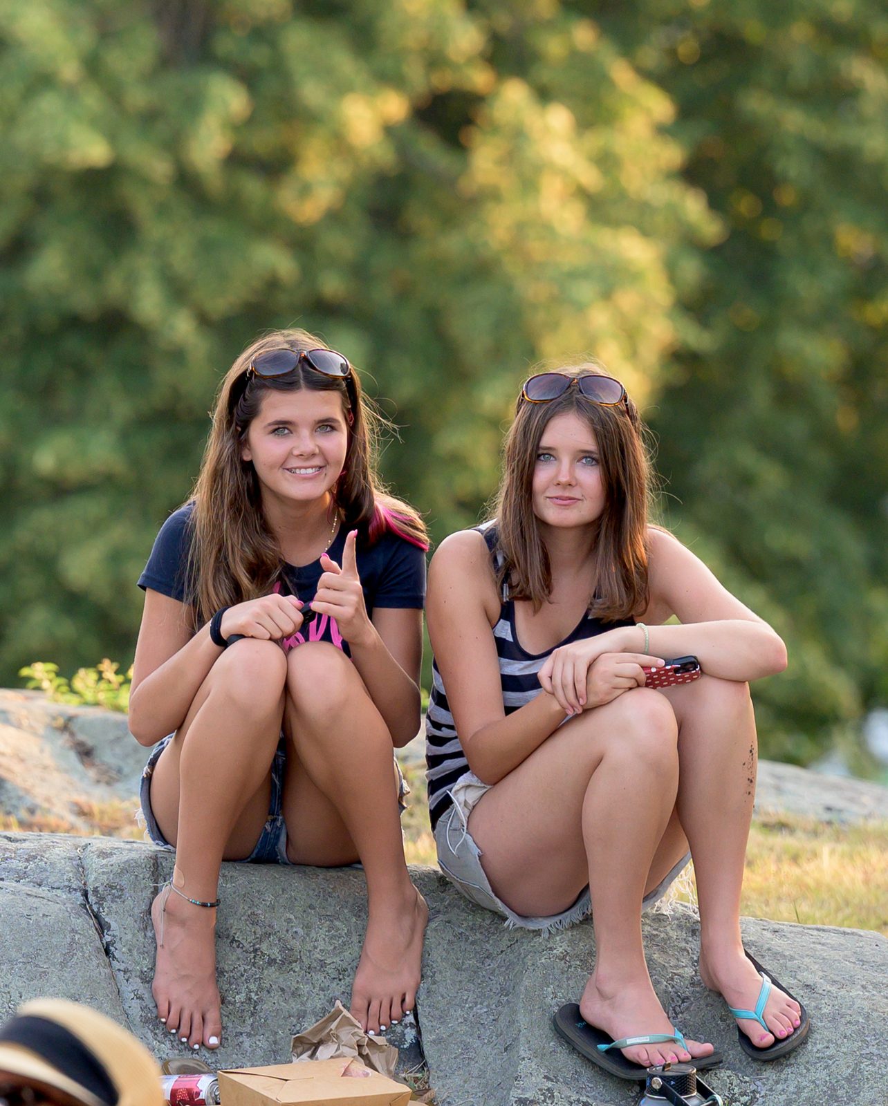 Two young festivalgoers pause from a picnic on the rocks to greet the camera.