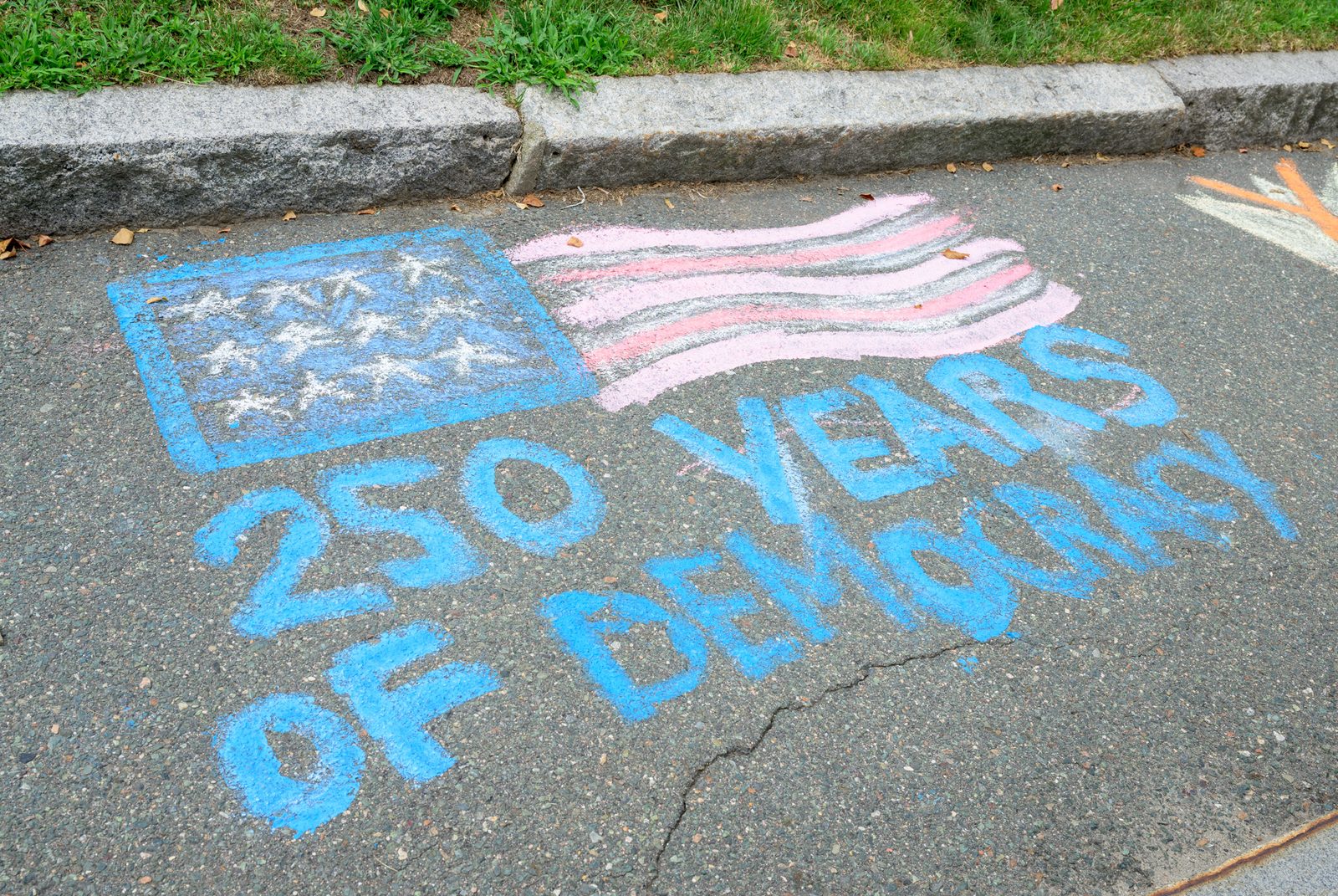 A chalk street painting of the American flag marks ‘250 Years of Democracy’ on the pavement.