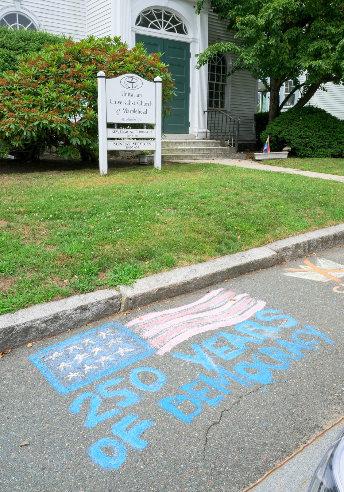 A chalk flag celebrating 250 years of democracy stretches across the street in front of the Unitarian Universalist Church of Marblehead, established 1716.