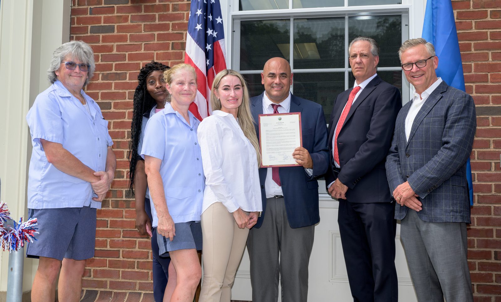 Marblehead Postmaster Chris King holds a signed proclamation marking 250 years of the U.S. Postal Service, joined by Select Board member Moses Grader and other postal workers and town officials outside the post office.