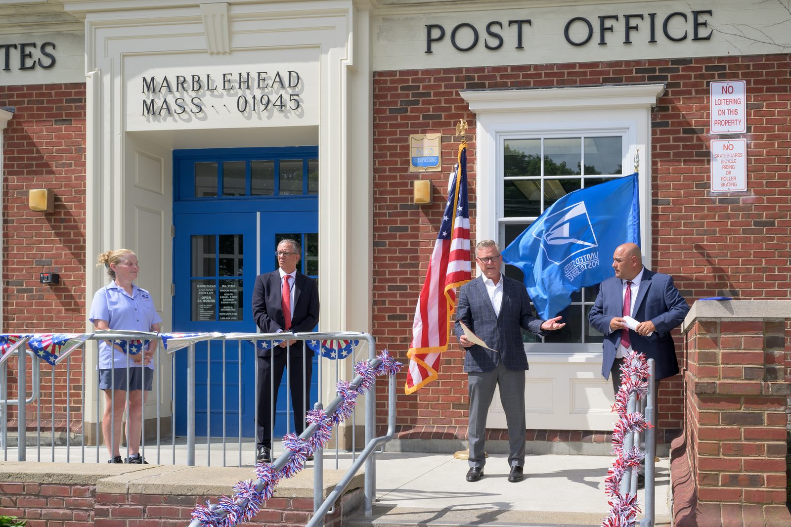Select Board member Moses Grader delivers remarks beside the American and U.S. Postal Service flags as Postmaster Chris King looks on.