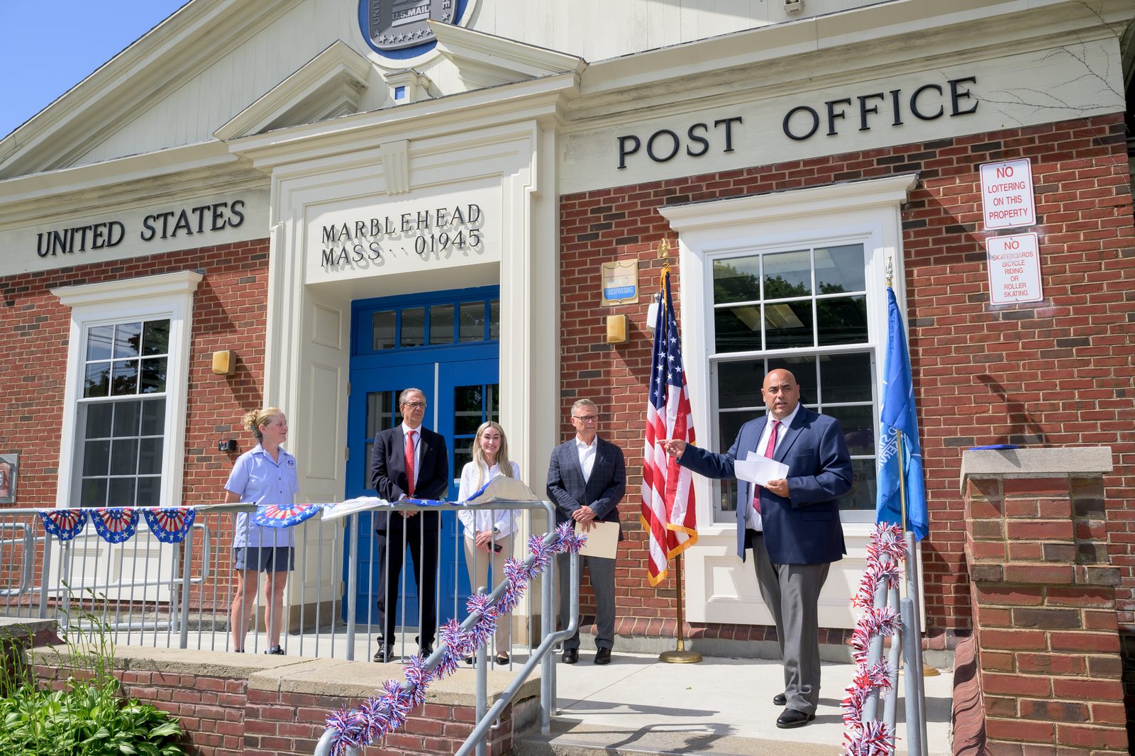 Postmaster Chris King gestures toward postal staff and guests lined along the railing during the ceremony.