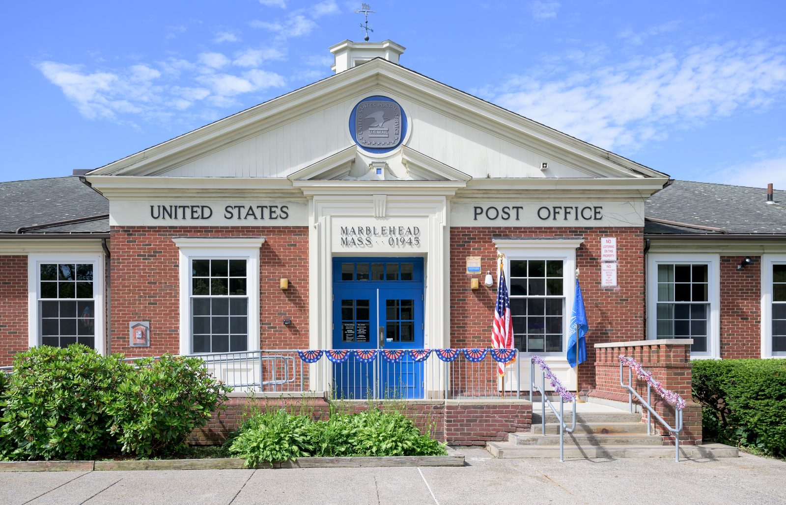 Patriotic bunting and flags dress the front of the Marblehead post office on Smith Street under a clear July sky.