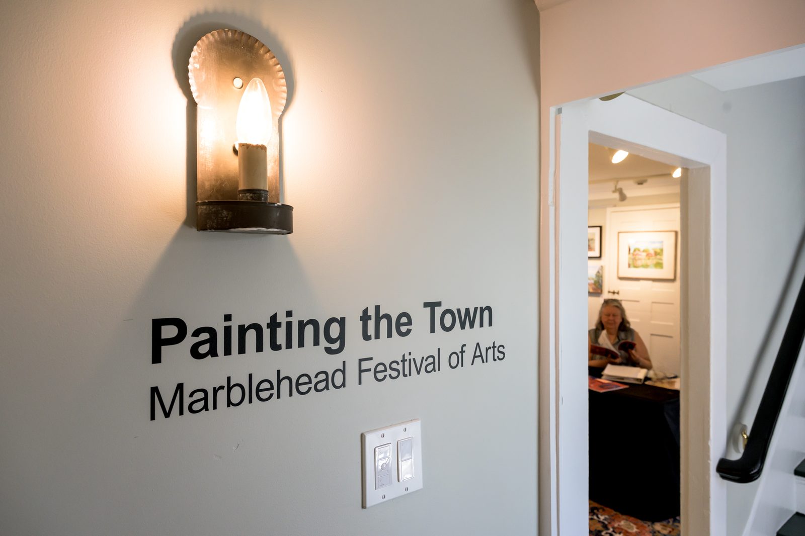 A wall sign points visitors to the Painting the Town exhibit as a volunteer keeps watch over the gallery.