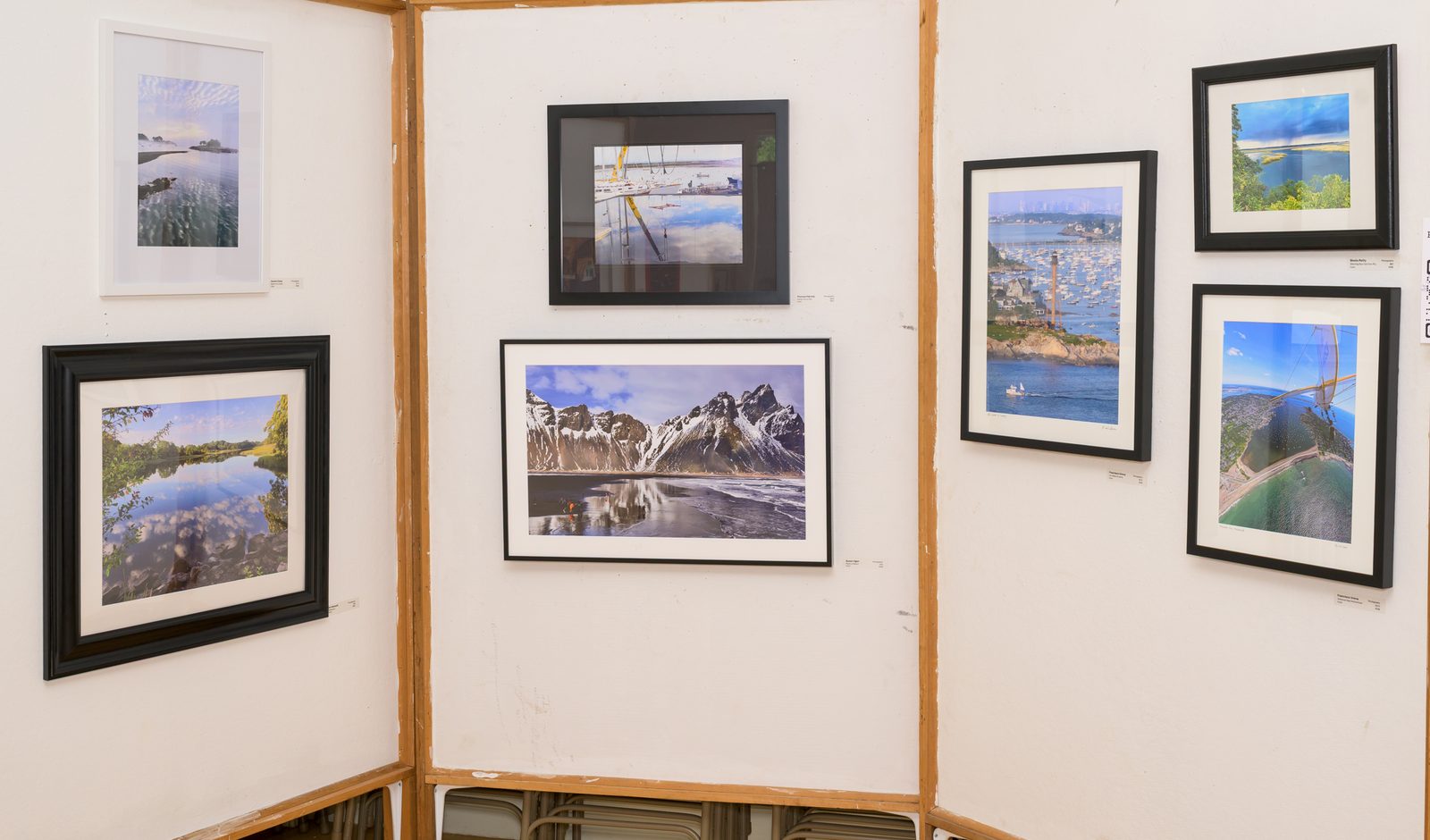 Framed landscape and harbor photographs hang on display panels in the photography exhibit.