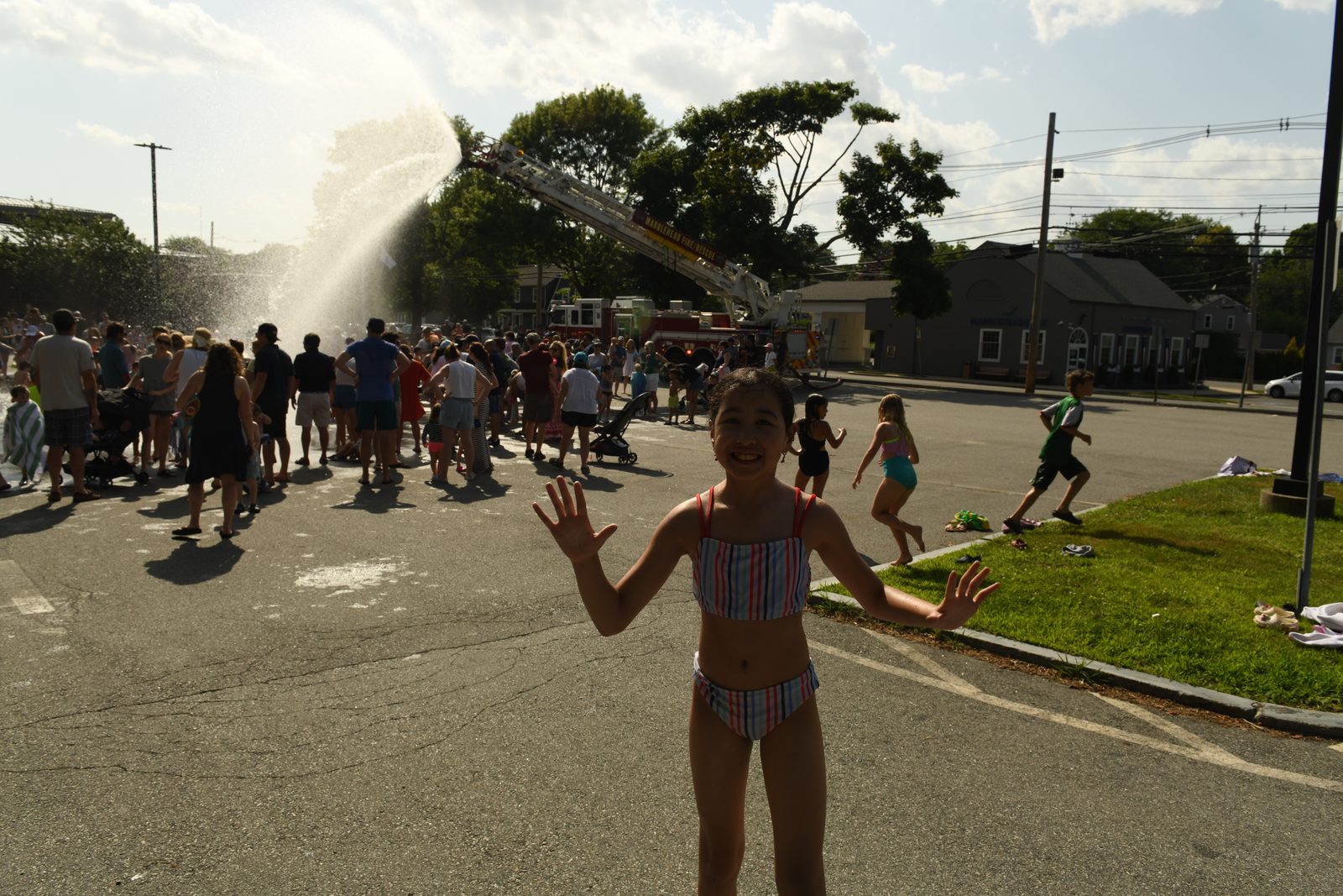 A girl throws both hands up toward the camera as kids run behind her.