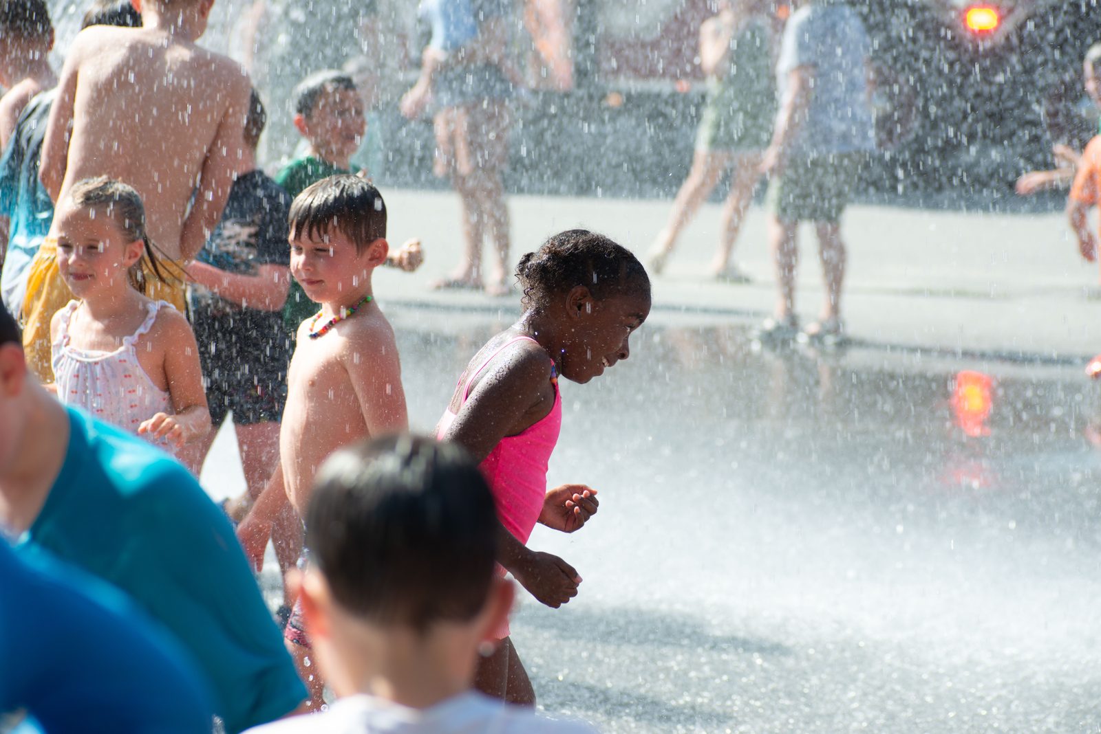A small girl in a pink swimsuit runs through the spray.
