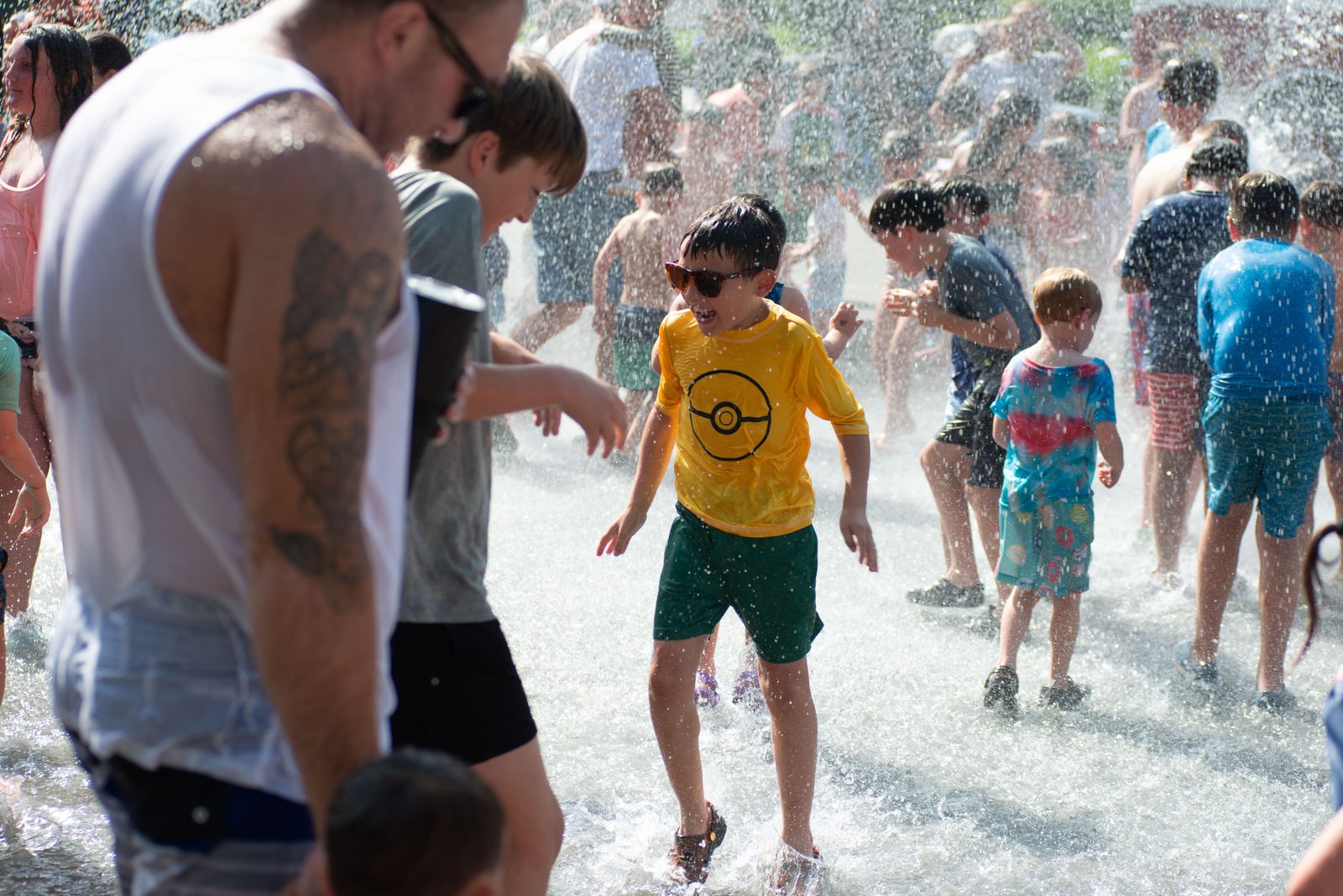 A father and a boy in a Pokémon shirt run through the water together.