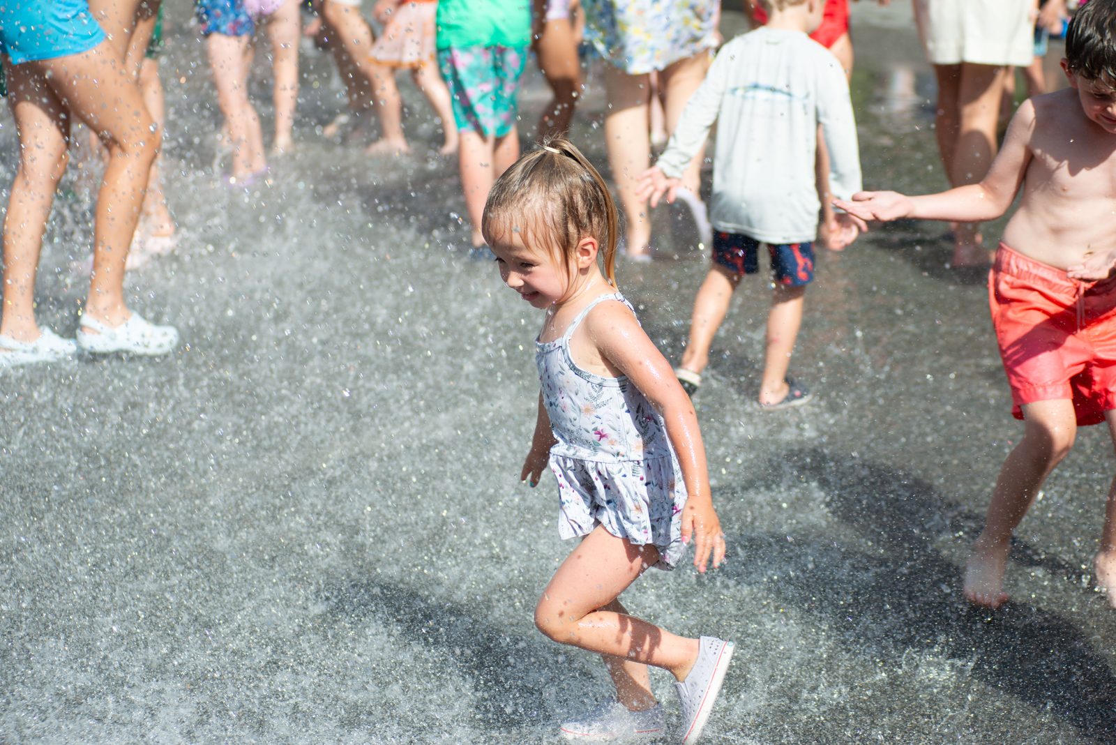 A toddler in a ruffled swimsuit dashes through the mist.