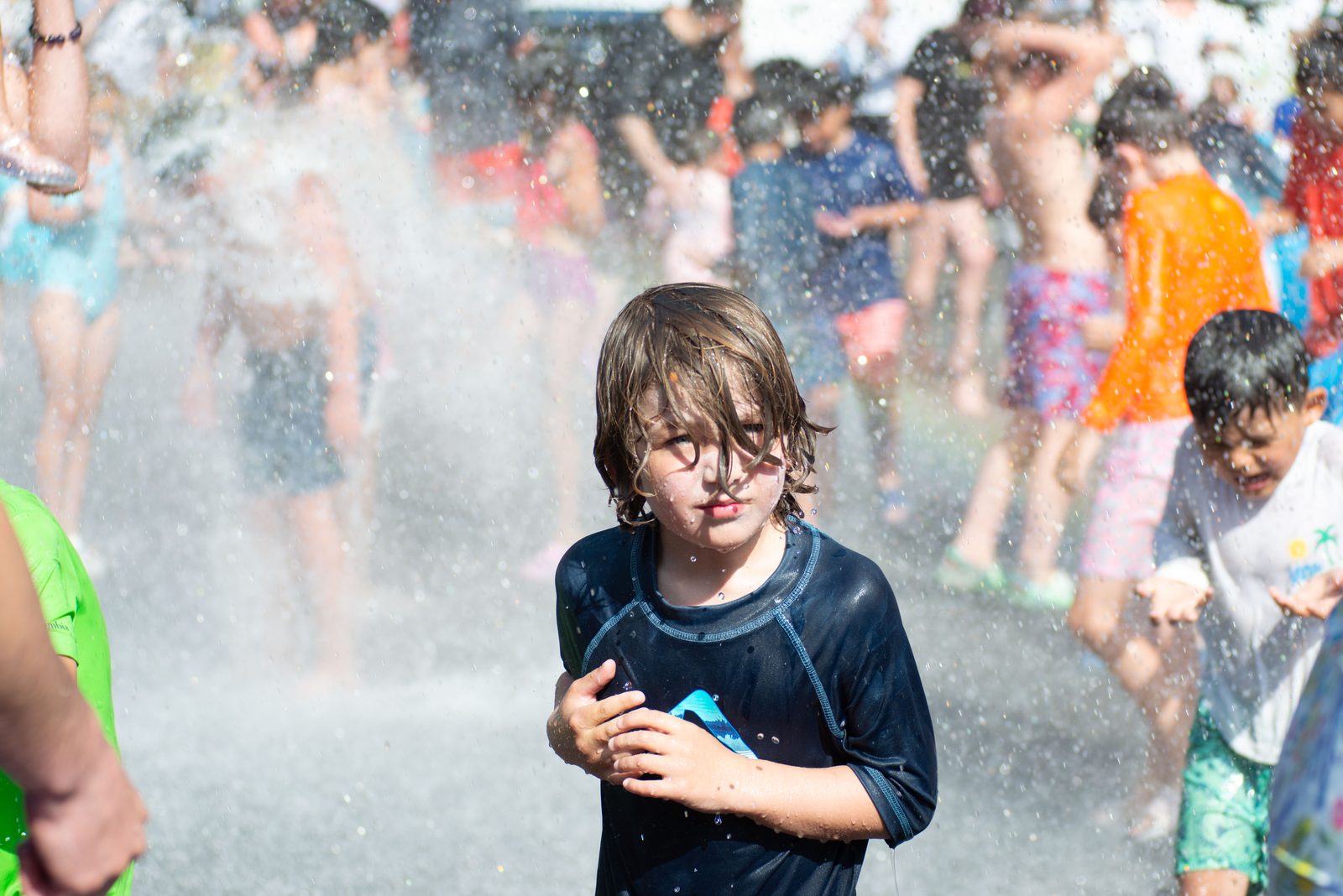 A boy in a soaked rash guard hugs himself against the sudden cold.