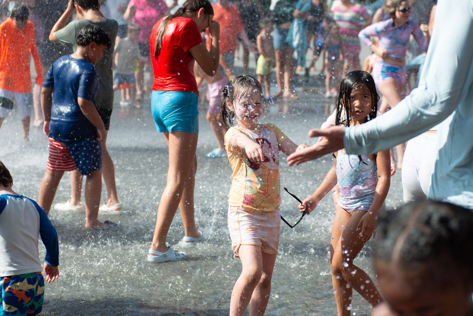 A girl clutches her sunglasses as she plays in the spray.