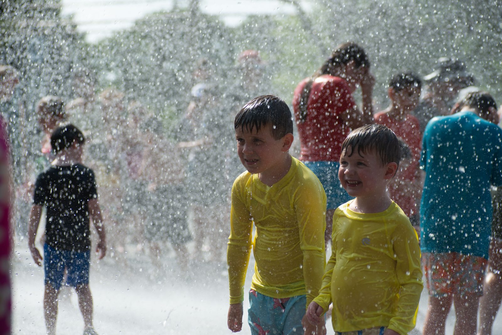 Two boys in matching yellow rash guards grin in the spray.
