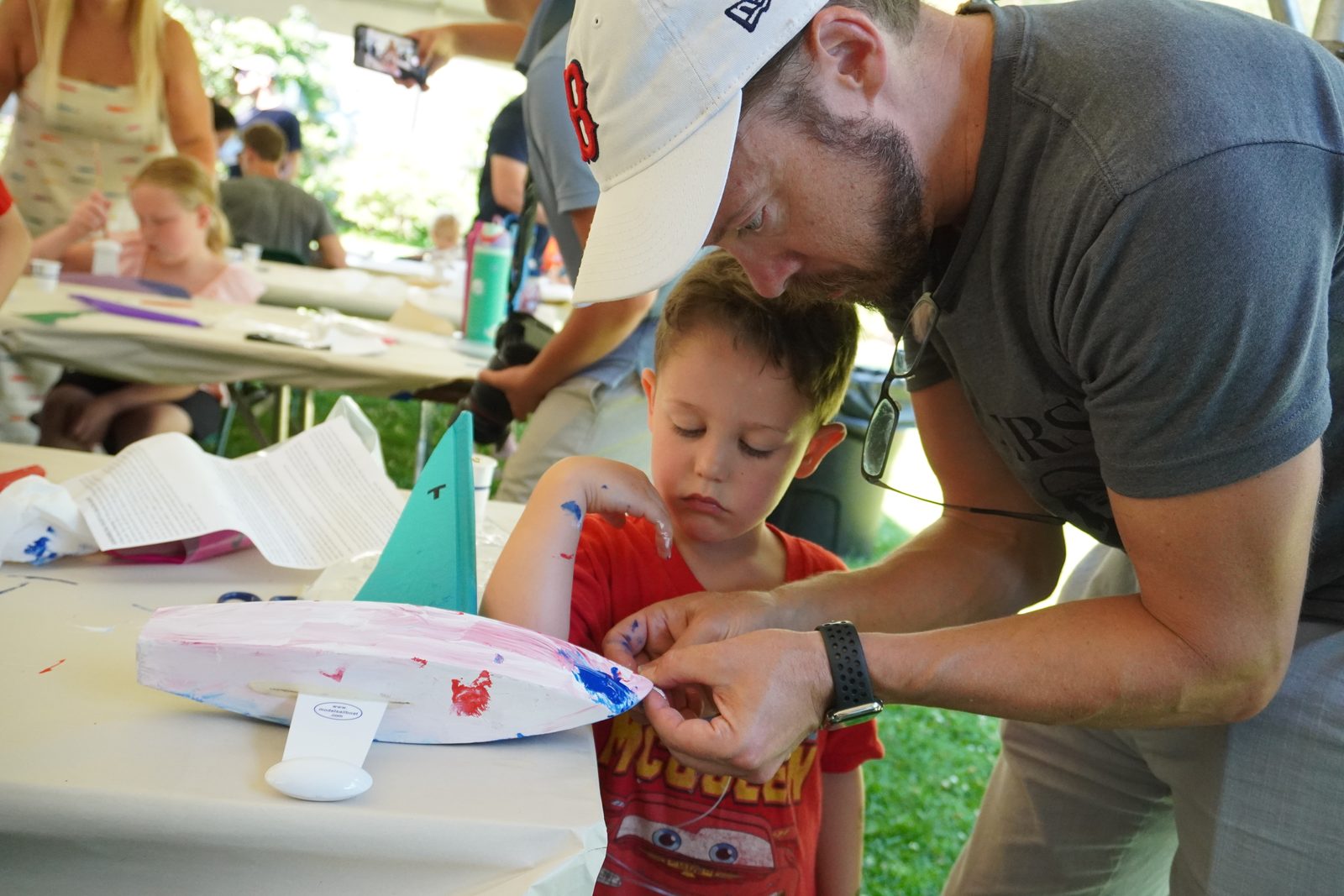 A father threads a sail onto his son’s freshly painted boat.
