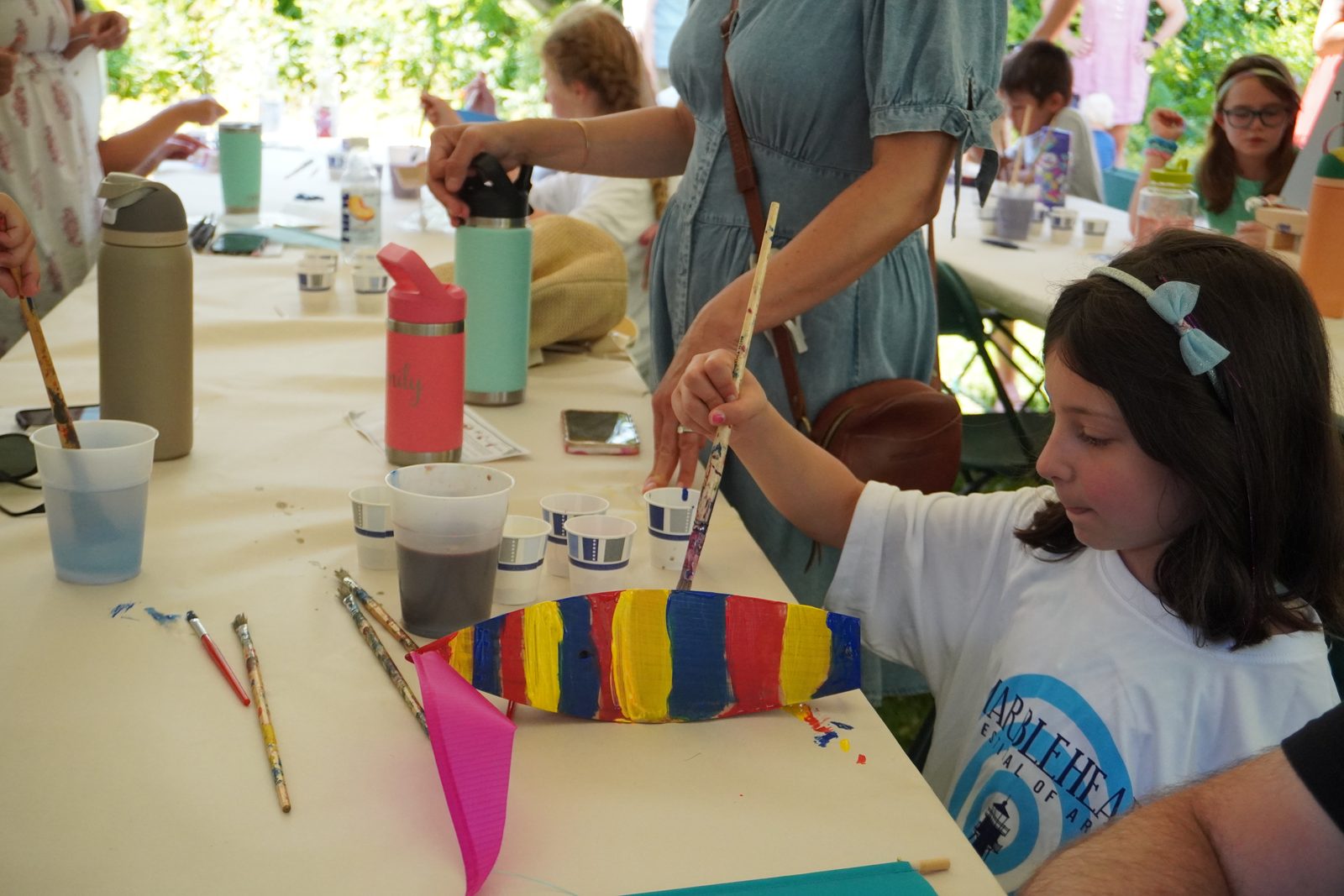 A girl brushes bold red, yellow and blue stripes across her boat.
