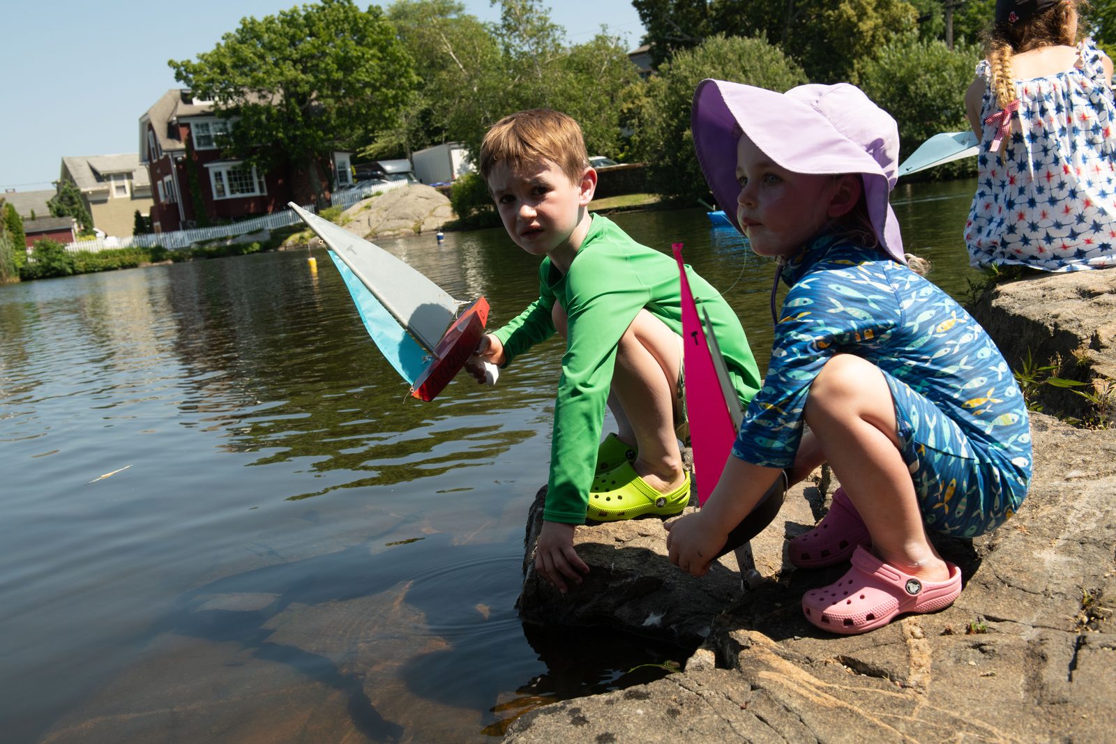 Two children crouch at the rocks to set a boat adrift.