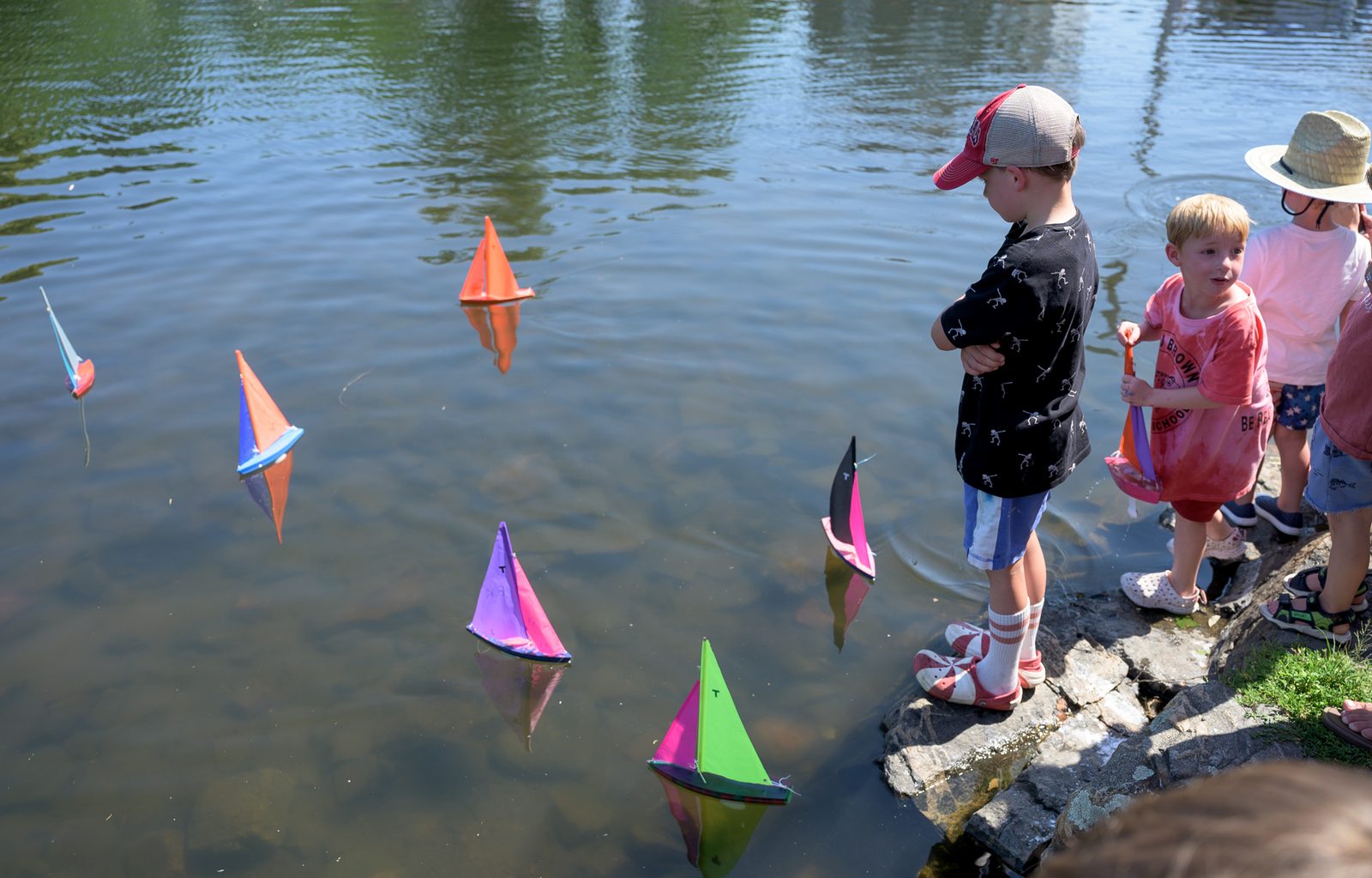 At the pond’s edge, young sailors nudge their boats out past the reeds.