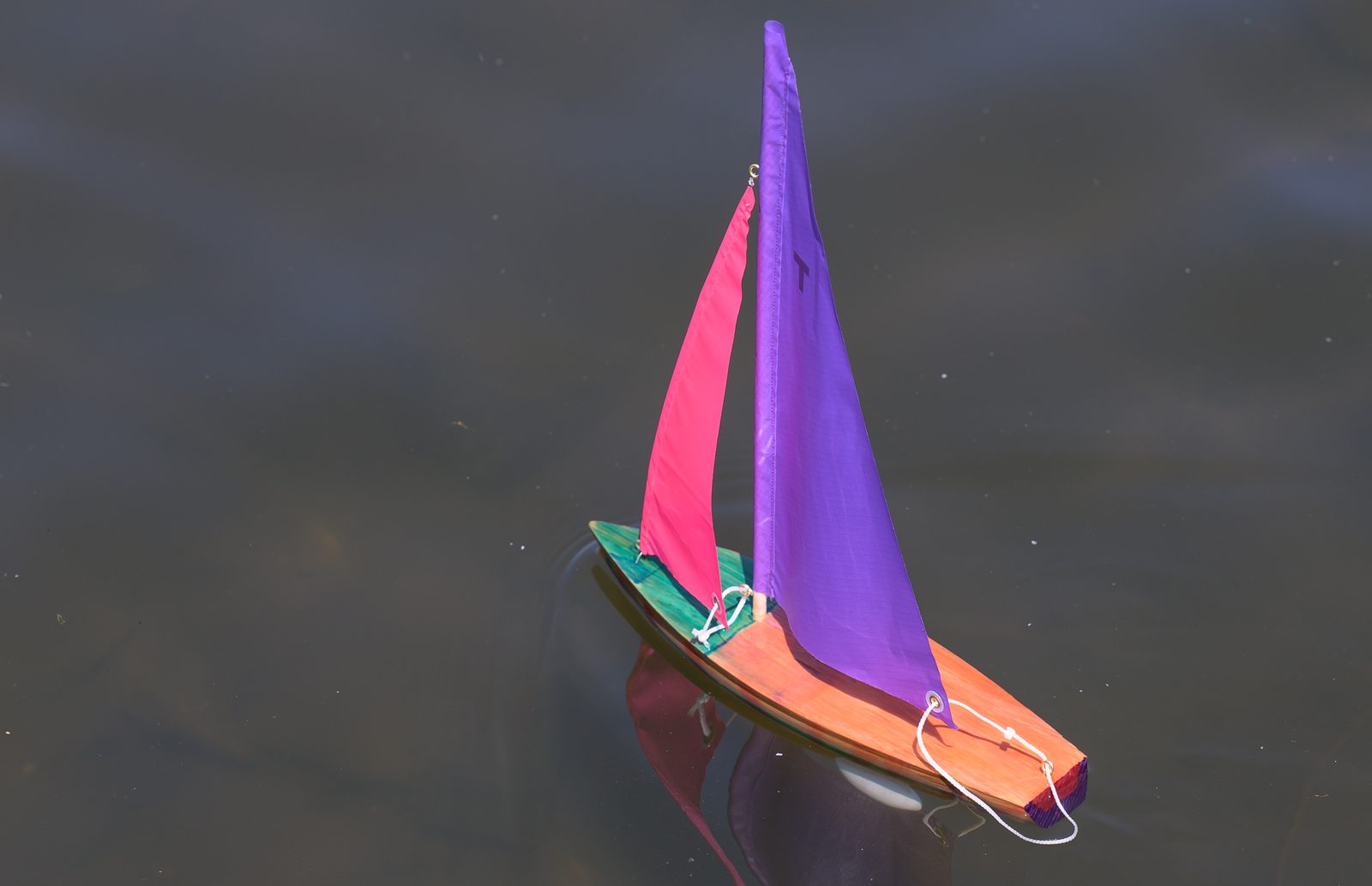 A single boat catches the wind and crosses the pond alone, its bright sails doubled in the still water.