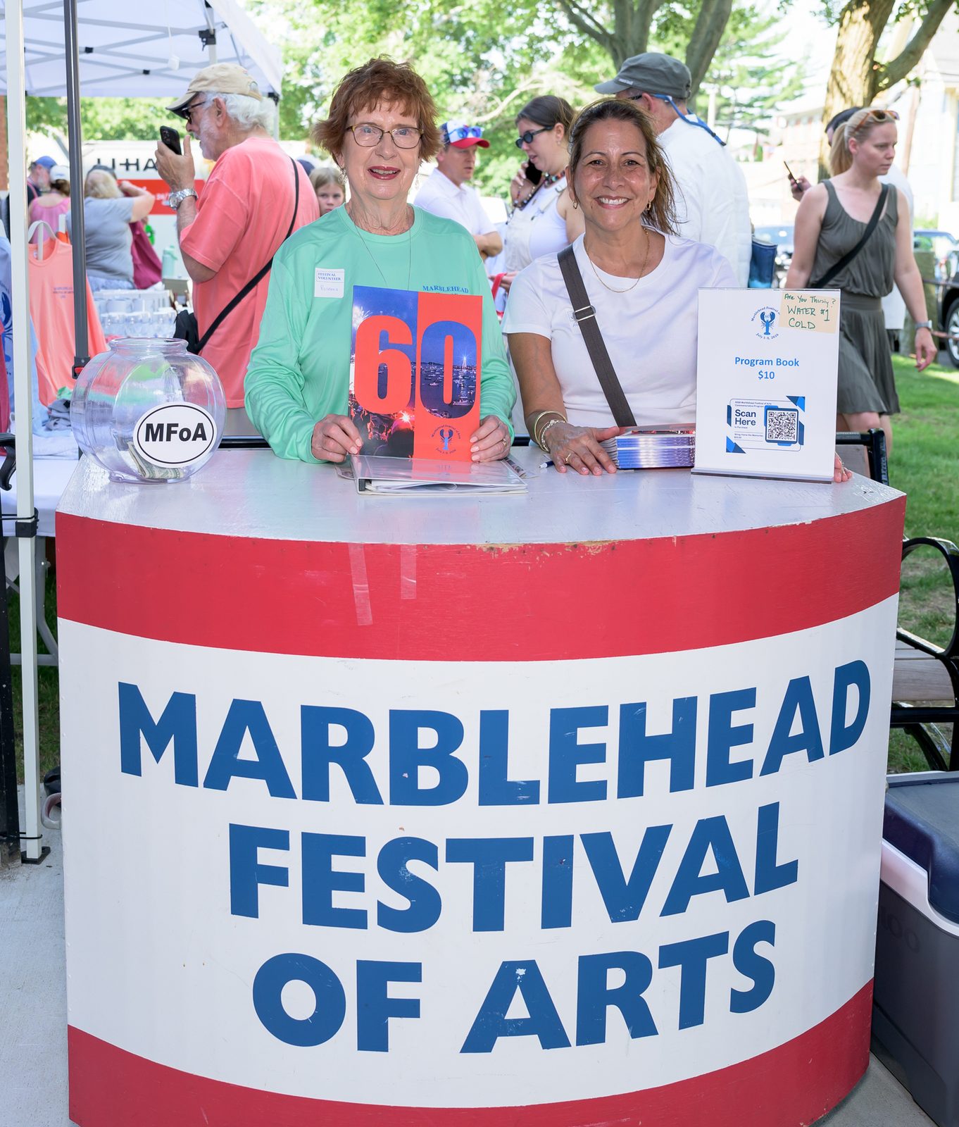 A festival volunteer holds up the sixtieth-anniversary program book at the information booth, where a glass jar collected donations for the Marblehead Festival of Arts.