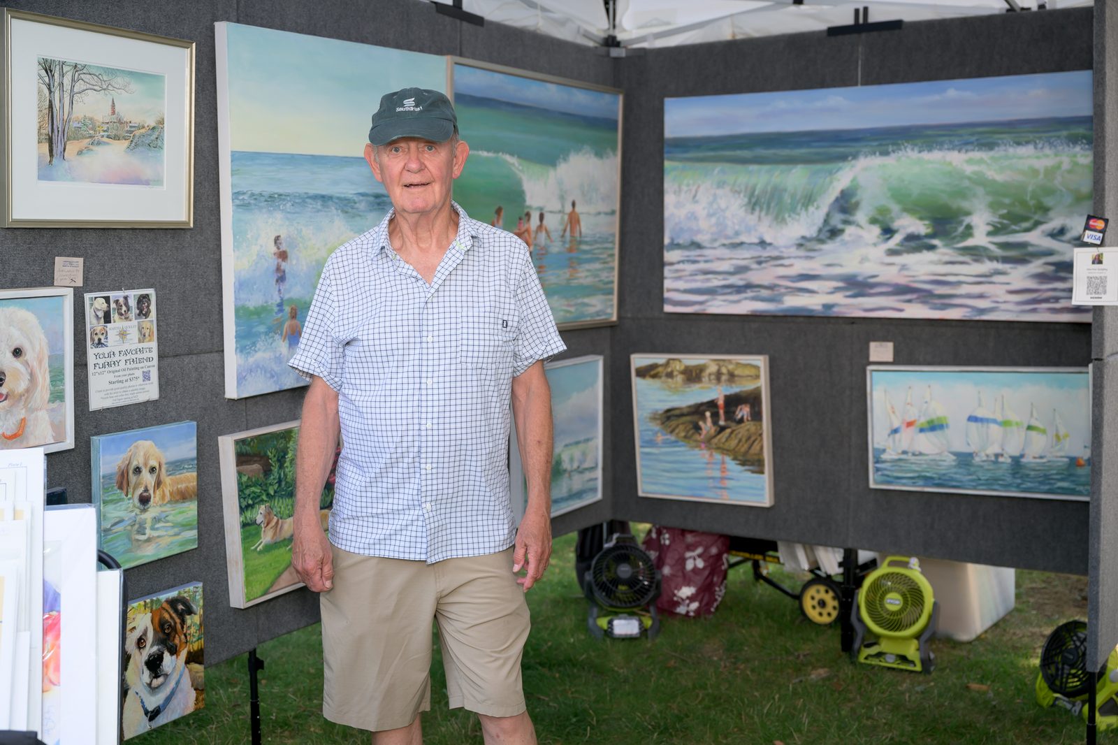 A painter stands among his booth of breaking-wave seascapes and commissioned pet portraits.