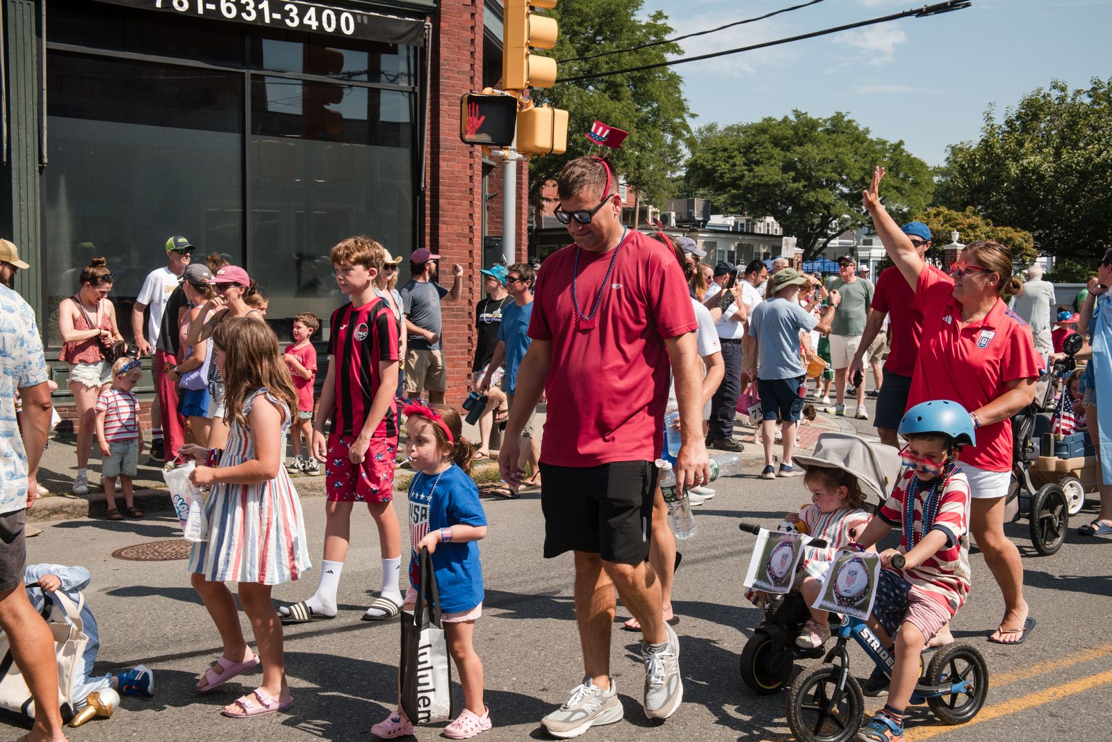 A family crosses the route, a girl in patriotic Mickey ears clutching a box of candy.