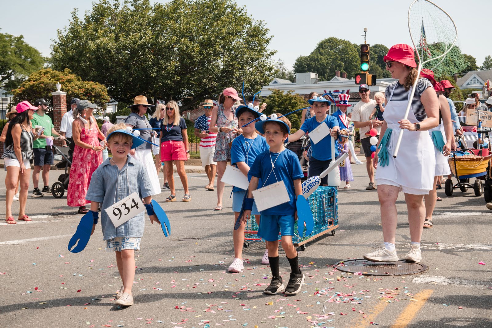 Children costumed as blue lobsters — ‘Lobster Legends’ — march with a lobster trap on a cart.