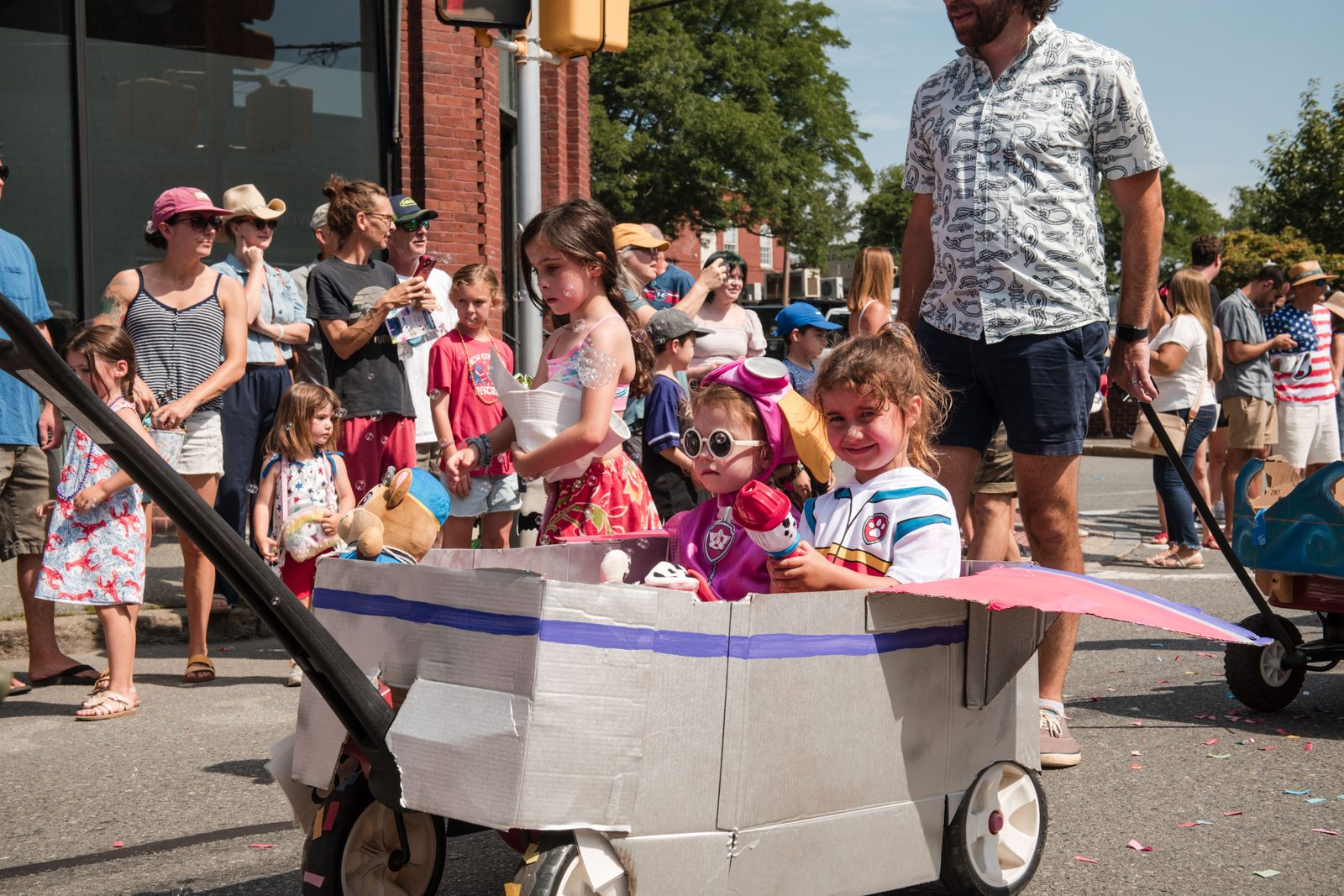 Two small children ride in a cardboard vehicle pulled down the parade route.