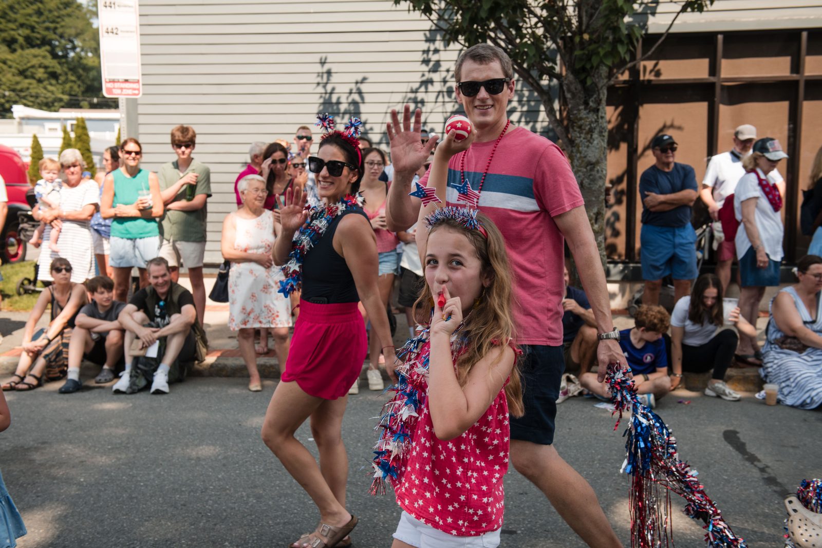 A woman holds a baby and a battery fan against the heat as the parade goes by.
