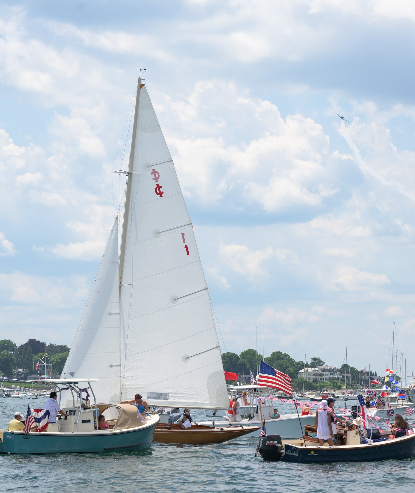 Decorated boats crowd the harbor as a plane trails smoke across the sky overhead.