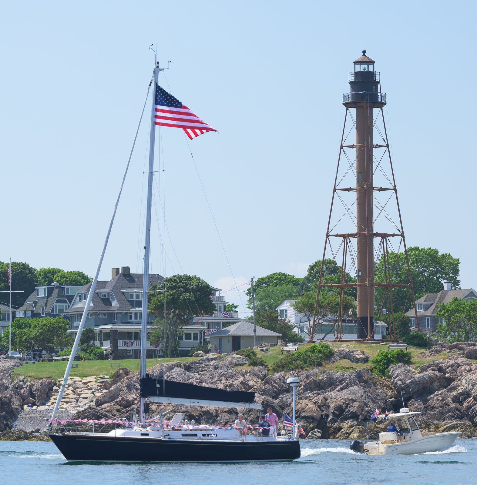 A sailboat under the Stars and Stripes passes Marblehead Light during the harbor parade.