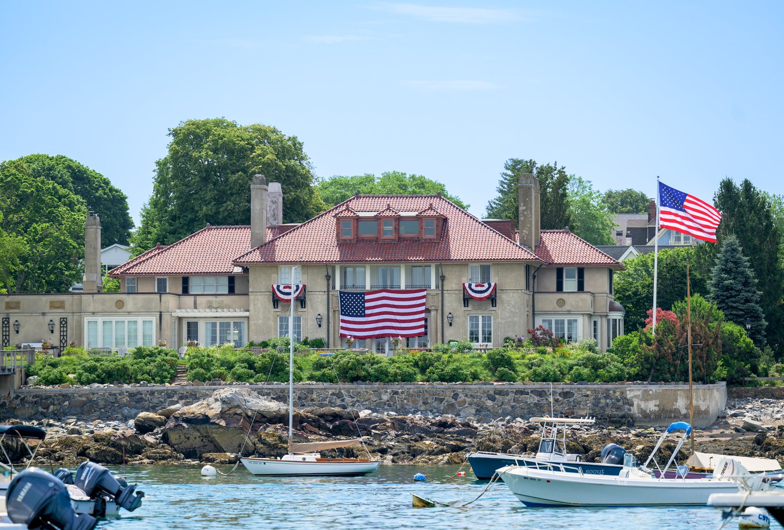 A waterfront house draped in a giant flag and bunting, seen from the water during the boat parade.