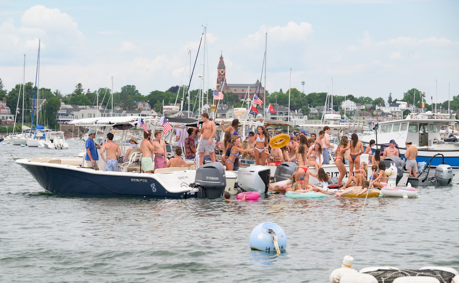Boats raft up off the shore during the harbor boat parade, Abbot Hall rising over the mooring field beyond.
