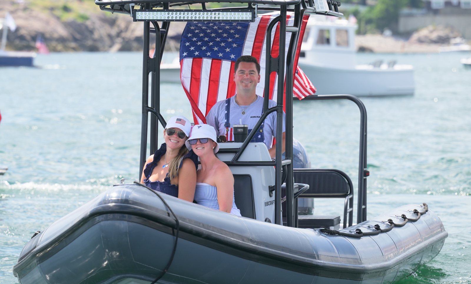 A crew rides an inflatable through the harbor under a large flag during the boat parade.