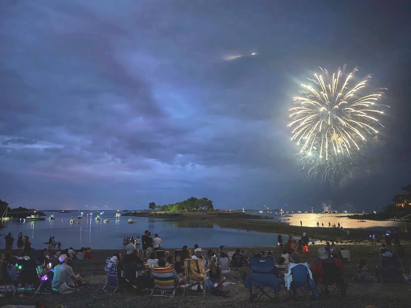 Half of Marblehead lines the beach as the first fireworks open over the harbor, the barge smoking at the water’s edge.