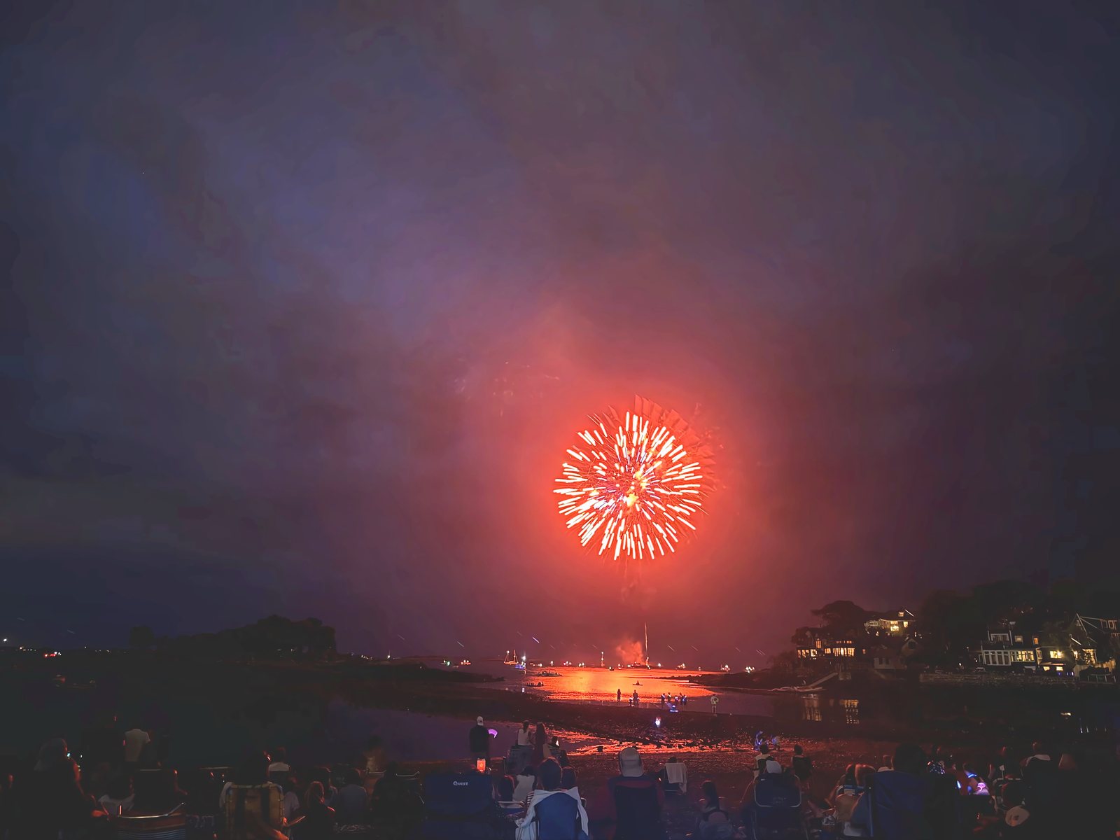 A big red burst turns the harbor and the low-tide flat crimson beneath it.