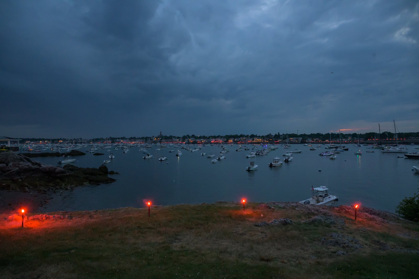 Red flares ring the shore for the harbor illumination as dusk falls over the moored fleet, Abbot Hall on the skyline beyond.